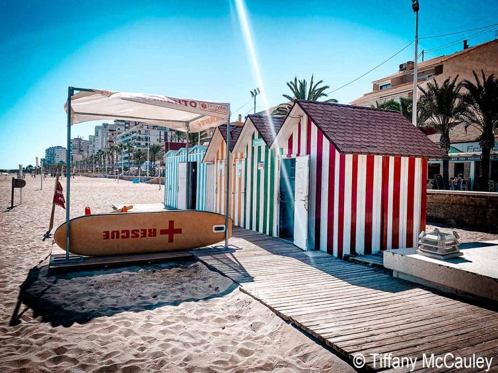 Beach huts and a surf board on the beach in El Campello, Spain.